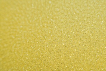 the texture and details of a kitchen sponge used for dishwashing. The sponge’s porous surface is clearly visible, showcasing its small, irregular holes and soft