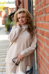 Side view portrait of beautiful smiling long haired caucasian blond woman in blank white sweater standing outdoor on city street by brick building on zebra crossing in autumn morning. Fashion theme.