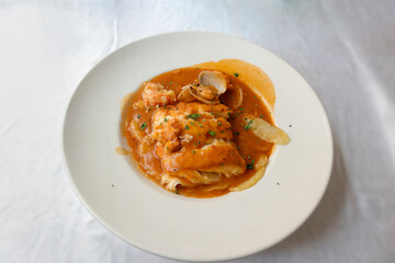Hake trunks with clams and sauce on a white plate on a white tablecloth
