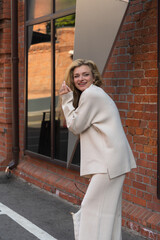 Portrait of beautiful happy long haired caucasian blond woman in white sweater with handbag walking or standing outdoors on city street by red brick loft building. Soft focus. Fashion and beauty theme