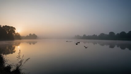 Fototapeta premium A golden sunrise illuminates the mist-covered lake, where a flock of birds glides over the calm water. The soft light and fog create a peaceful and ethereal scene, highlighting the beauty of nature at
