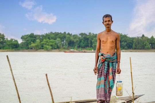 Riverside people of Bangladesh. A fisherman stands in the twilight horizon behind the river bank.