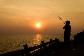 Silhouette young man fishing on a  sea during at sunrise.