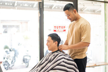 Fototapeta premium A man is currently enjoying the experience of getting his hair cut by a skilled barber inside a bustling barber shop that is welllit