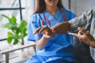 Smiling doctor is holding the hand of her senior patient during a home visit, providing support and...