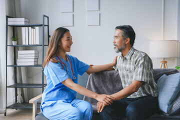Young female nurse wearing blue scrubs is comforting a senior male patient on the sofa during a home visit