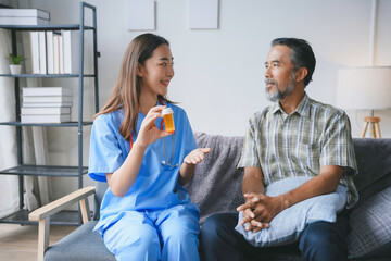 Young smiling nurse is holding a pill bottle and explaining how to take medicine to a senior patient at home