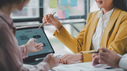 Business team working together, analyzing financial data on a tablet and discussing a summary report using a pen to point at the screen