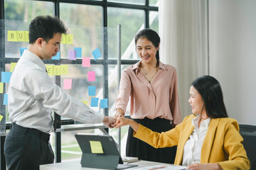 Three asian business people putting their fists together celebrating a business goal achievement in the office