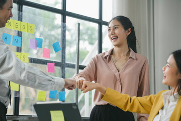 Team of young professionals is celebrating success with a fist bump in their modern office, showcasing teamwork and achievement