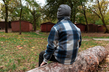 A small boy in a plaid shirt sits on a felled tree against an old iron garages