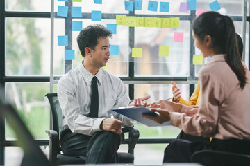 Business team brainstorming and sharing new project ideas using sticky notes on glass wall in the meeting room