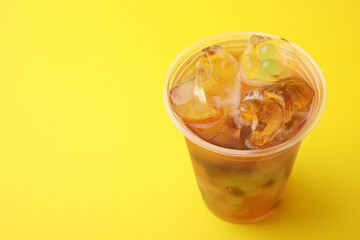 Tasty bubble tea in plastic cup on yellow background, closeup. Space for text