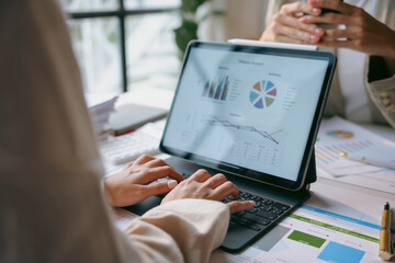 Businesswoman analyzing financial charts and graphs displayed on a tablet computer while working with colleagues in the office