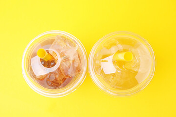 Tasty bubble tea in plastic cups on yellow background, flat lay
