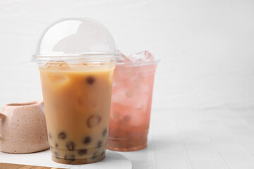 Tasty bubble tea in plastic cups on white tiled table, space for text
