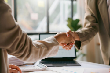 Two businesswomen shaking hands after closing a deal in their office with a laptop and calculator...