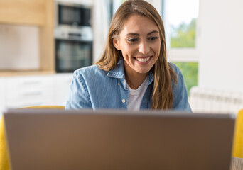 Young woman working on laptop at home in front of kitchen