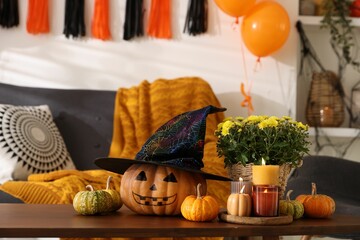 Burning candles, flowers and pumpkins on table in room decorated for Halloween