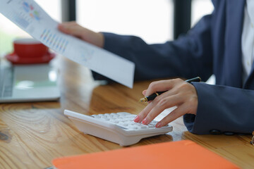 Close-up of businesswoman's hands using a calculator to check company finances, earnings, and budget. The accountant calculates monthly expenses, papers, loan documents, and invoices.