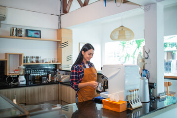 Indonesian waitress making coffee using a coffee maker in a coffee shop kitchen