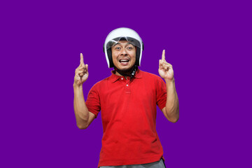 Young Asian driver man wearing helmet looking up while raising both hands and pointing upwards with happy expression
