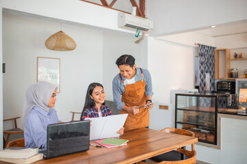 male waiter using a pad serving two female customers holding a menu list at a coffee shop