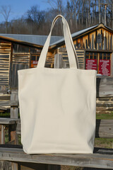A plain white tote bag displayed outdoors against a rustic wooden backdrop.