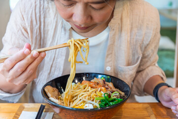 Woman eating a ramen Japanese noodle soup in a black color ramen bowl.