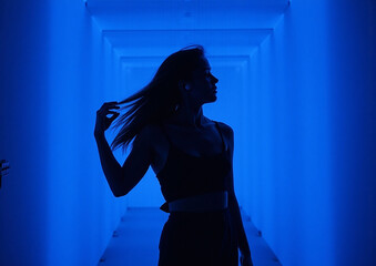 Futuristic Silhouette of Person Wearing Wireless Earbuds in Dramatic Blue Lighting with Abstract Artistic Pose