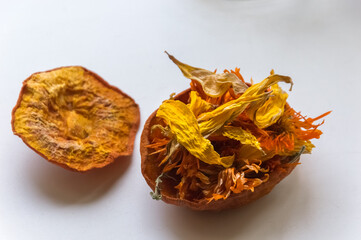 Dried calendula flowers in a bowl of dried pumpkin on a white background.