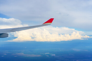 Wing view from the airplane window at beautiful cloudy fluffy thunderstorm clouds sky and the airplane wing