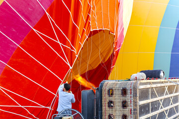 Hot air balloon with flame and basket lying on the ground on the field while filling with air and...