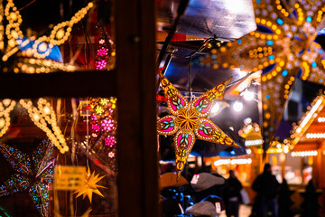 Rain speckled window showcasing illuminated colorful star lanterns glowing at Berlin Christmas market. Festive winter atmosphere with vibrant holiday lights