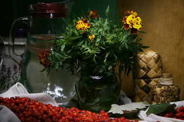 Still life with marigolds in a jar of water, surrounded by kitchen utensils.
