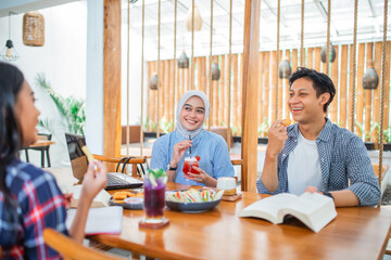 three students eat snacks and drink and chat while working assignments at a cafe