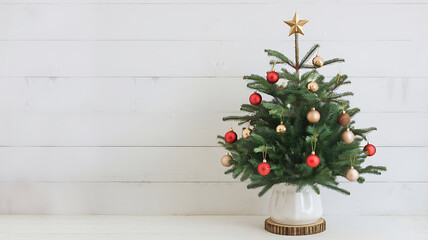 Fototapeta premium Minimalist Christmas tree with red and gold ornaments on white wood background for holiday design. 