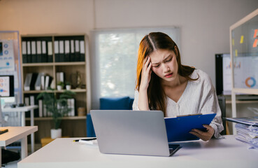 Stressed young businesswoman in office, tired, holding head, overwhelmed by work, feeling deadline pressure