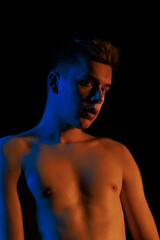 Fototapeta premium Young man posing in the dark with red and blue light in the studio