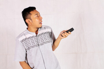 Asian man holding tv remote with surprised and confused expression
