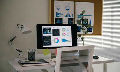 Clean and organized home office with a computer showing data analysis on the screen. The desk is white with a white chair, a lamp, and office supplies