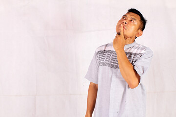 Mature Asian man thinking with pensive expression wearing blue shirt with hand on chin
