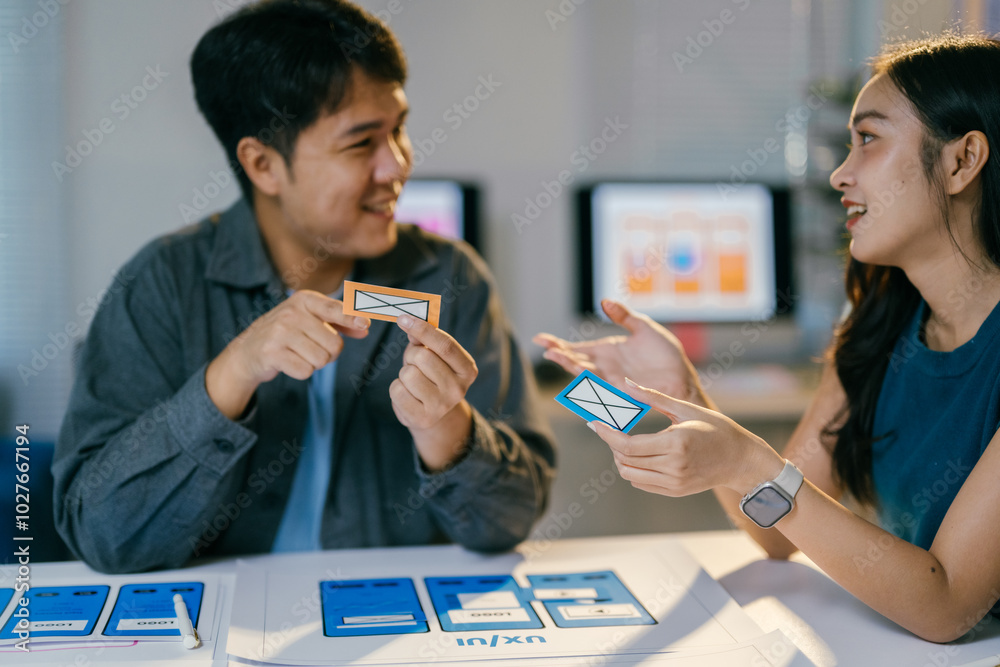 Leinwandbilder Two asian ui/ux designers discussing user interface in a modern office filled with creativity and collaboration. Smiling and sharing ideas, showcasing teamwork in web and app development