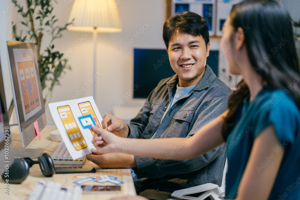 Poster two asian ui/ux designers happily discuss a mobile app wireframe in their office, brainstorming and 