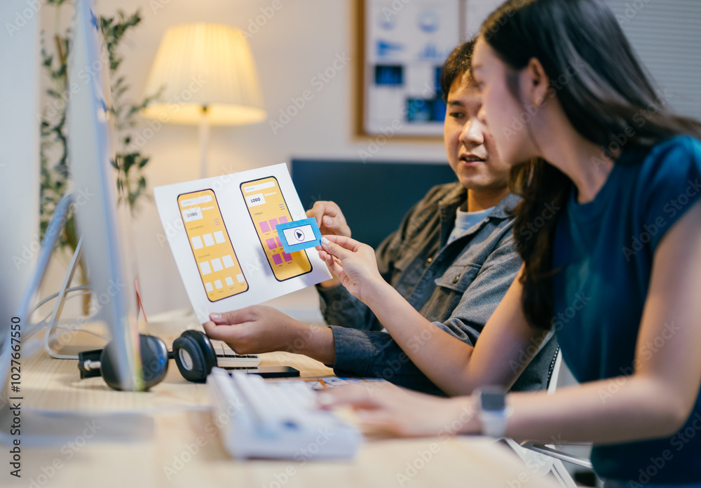 Aufkleber Two asian ui/ux designers are discussing a mobile app wireframe prototype at their desks in the office, improving the user experience with every iteration