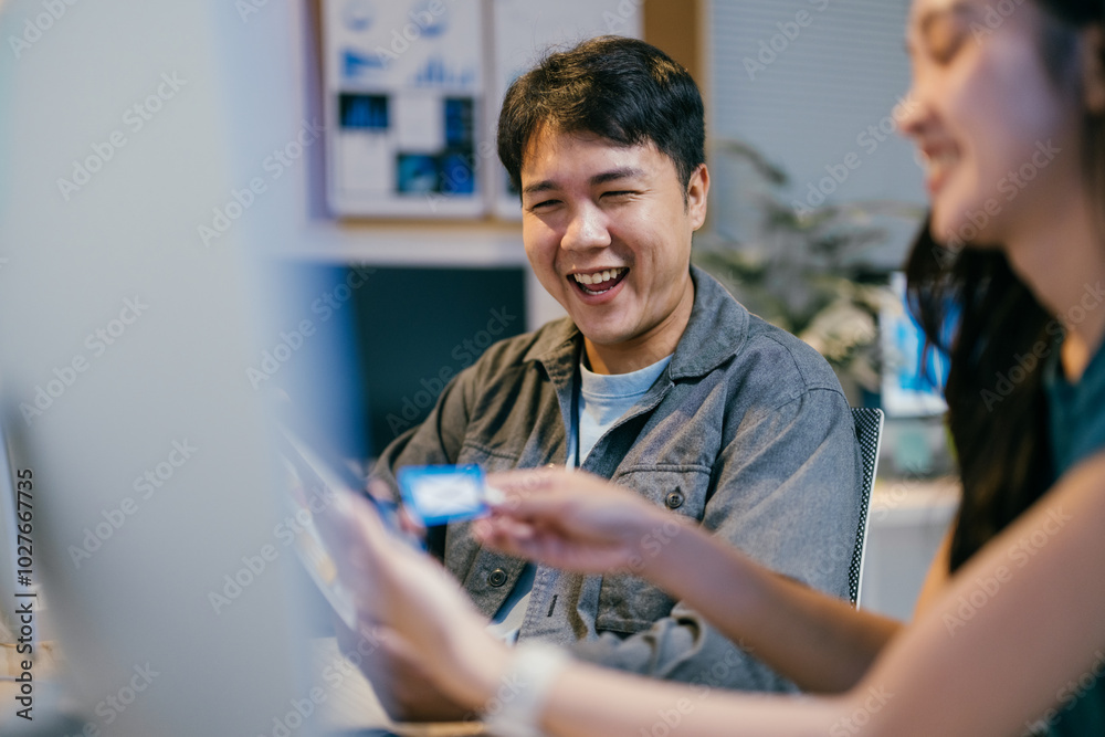 Poster Two software developers are having fun while working together in the office. They are looking at a funny meme on a smartphone