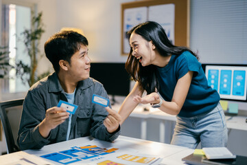 Two asian ui ux designers are working and having fun in the office, designing the user interface and experience of a mobile application