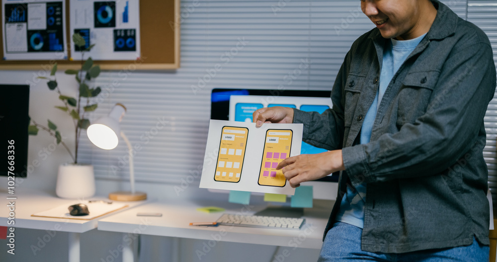 Aufkleber Asian ui designer is comparing two different versions of a mockup for a mobile phone app while working in his office