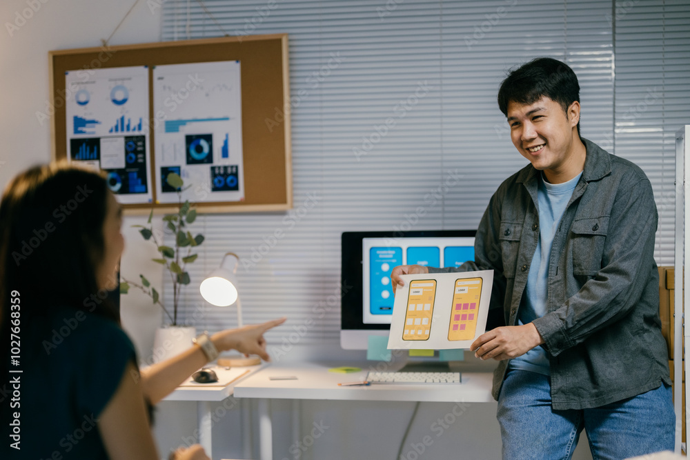 Poster Two asian ui/ux designers collaborate in a modern office, discussing a mobile app interface