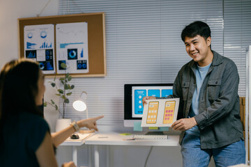 Two asian ui/ux designers collaborate in a modern office, discussing a mobile app interface